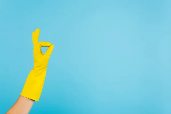 Vista parziale di casalinga in guanto di gomma giallo mostrando gesto ok isolato su blu — Foto stock