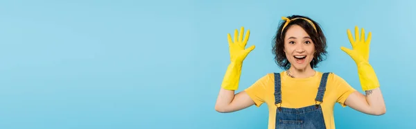 Erstaunt Hausfrau zeigt Hände in gelben Gummihandschuhen isoliert auf blau, Banner — Stockfoto