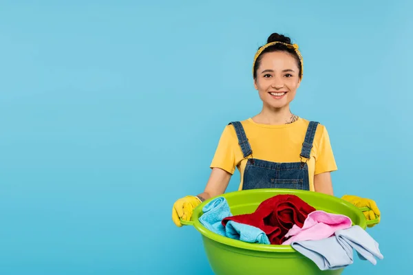 Donna elegante e allegra con la ciotola del bucato sorridente alla macchina fotografica isolata sul blu — Foto stock