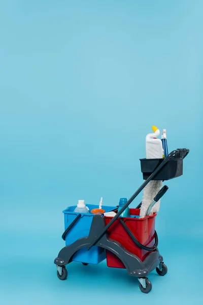 Cart with different cleaning supplies and buckets on blue background — Stock Photo