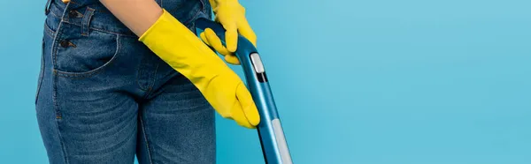 Vista ritagliata di casalinga in guanti di gomma gialla utilizzando aspirapolvere isolato su blu, banner — Foto stock