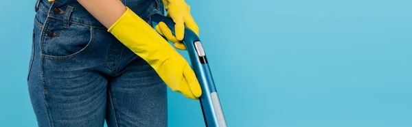 Vista recortada de ama de casa en guantes de goma amarilla utilizando aspiradora aislada en azul, pancarta - foto de stock