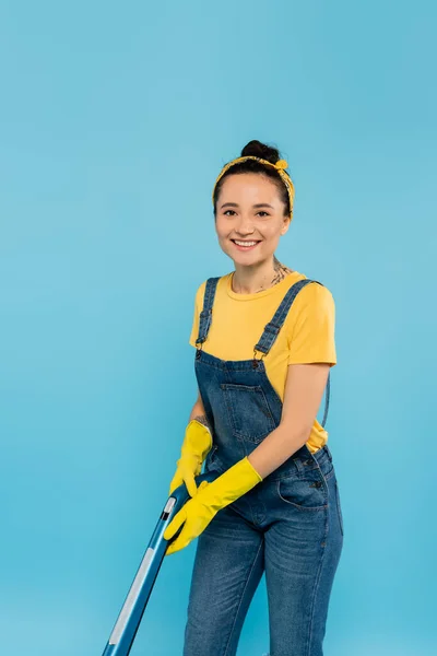 Femme au foyer gaie avec aspirateur souriant à la caméra isolée sur bleu — Photo de stock