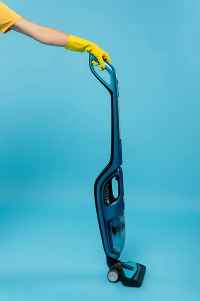 Cropped view of housewife in yellow rubber glove holding modern vacuum cleaner on blue — Stock Photo