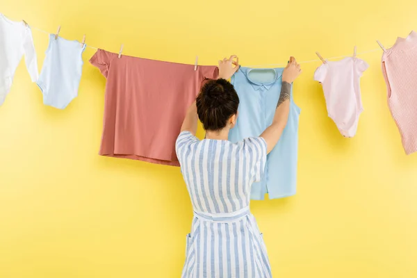 Rückseite der brünetten Hausfrau hängende Wäsche auf Seil auf gelbem Hintergrund — Stockfoto