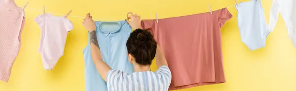 Vista trasera de la mujer tatuada colgando la ropa en la cuerda sobre el fondo amarillo, pancarta - foto de stock