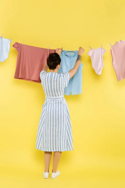 Back view of brunette woman near rope with laundry on yellow background — Stock Photo