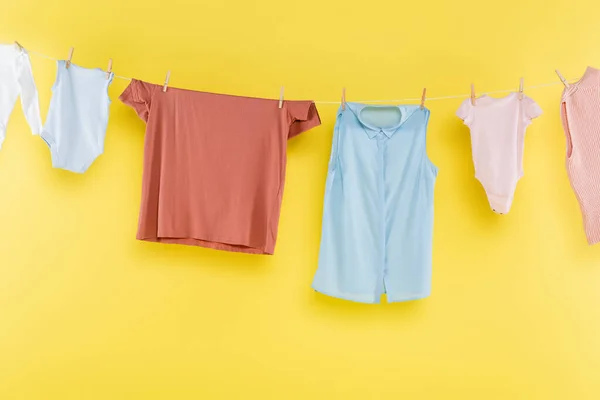 Roupas diferentes penduradas na corda no fundo amarelo — Fotografia de Stock