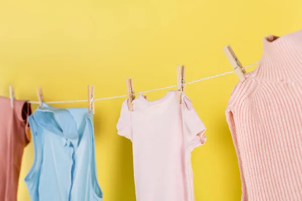 Blurred laundry hanging on rope with clothes pins on yellow background — Stock Photo