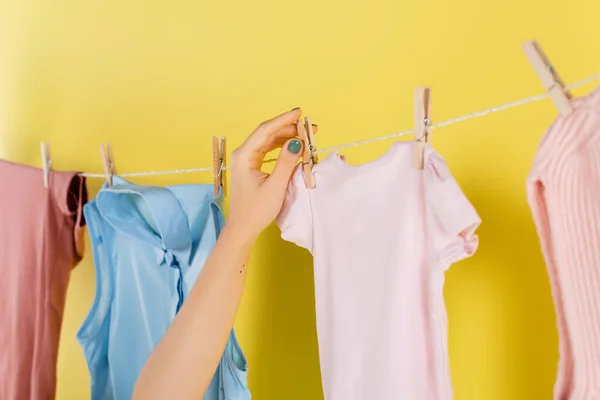 Corte vista de dona de casa pendurado roupas na corda no fundo amarelo — Fotografia de Stock