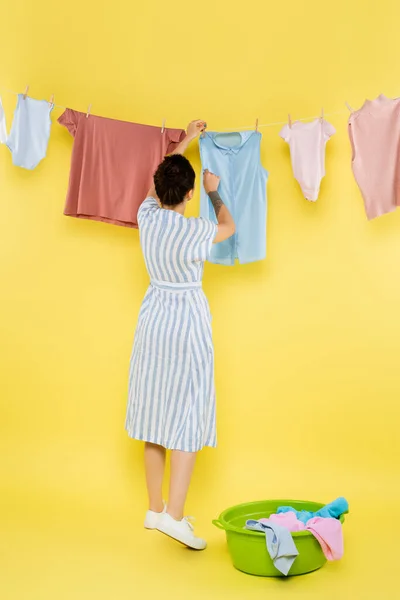 Vue arrière de la femme au foyer accrochant des vêtements sur corde sur fond jaune — Photo de stock