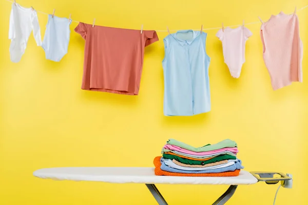 Clean clothes hanging on rope over ironing board on yellow background — Stock Photo