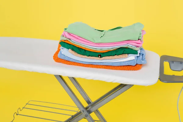 Stack of clean laundry on ironing board isolated on yellow — Stock Photo