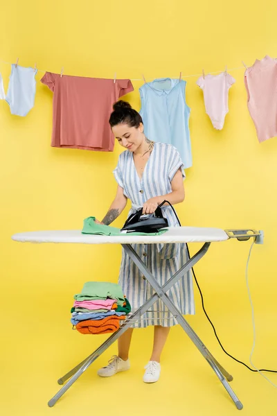 Sorridente casalinga stiratura vestiti vicino appeso lavanderia sul giallo — Foto stock