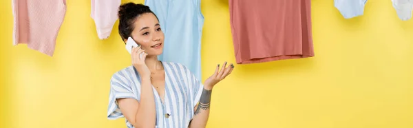 Tätowierte Frau spricht auf Smartphone neben Wäsche, hängt an Seil auf gelbem Hintergrund, Banner — Stockfoto