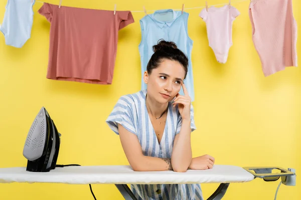 Nachdenkliche Hausfrau schaut bei Bügeleisen weg und hängt Wäsche an gelb — Stockfoto