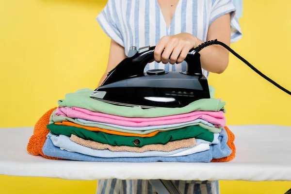 Cropped view of housewife with iron near clothes on ironing board on yellow — Stock Photo