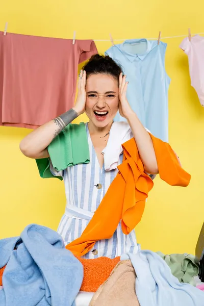 Irritated housewife touching head while screaming near laundry on yellow background — Stock Photo