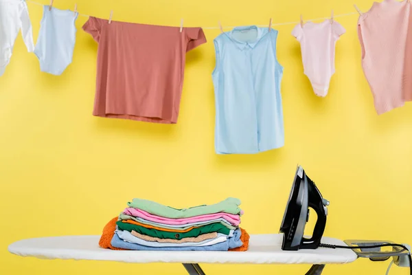 Clean clothes hanging over ironing board on yellow background — Stock Photo
