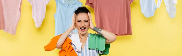 Shocked housewife touching head and screaming near laundry on yellow background, banner — Stock Photo