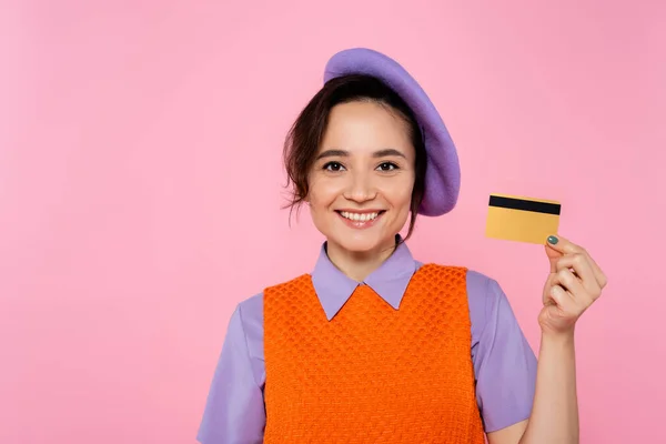 Mulher alegre e na moda mostrando cartão de crédito enquanto sorrindo para a câmera isolada em rosa — Fotografia de Stock