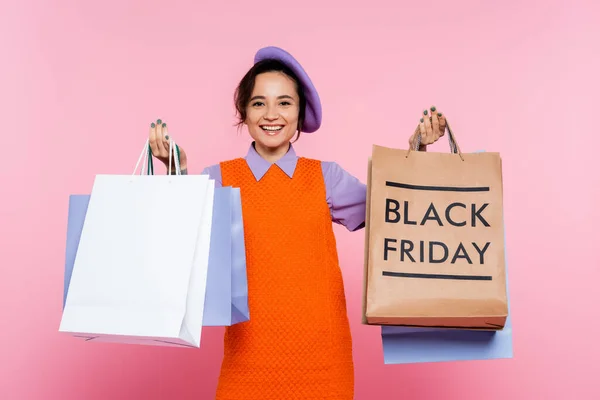 Mulher alegre em vestido sem mangas laranja segurando sacos de compras sexta-feira preto isolado em rosa — Fotografia de Stock
