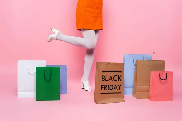 Vista parcial de la mujer cerca de bolsas de compras multicolores y letras de viernes negro en rosa - foto de stock