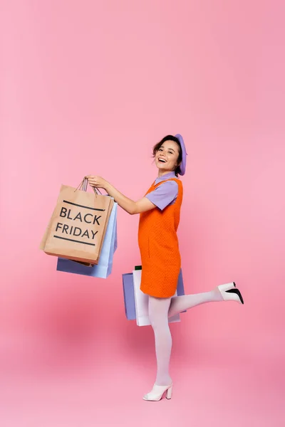 Mulher animado posando com compras e saco de compras com letras sexta-feira preto em rosa — Fotografia de Stock