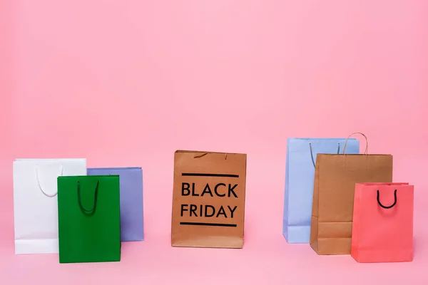 Bolsas de compras multicolores y letras de viernes negro sobre fondo rosa - foto de stock