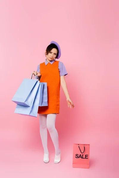 Femme bouleversée avec des achats pointant vers le sac à provisions avec lettrage de vente sur rose — Photo de stock