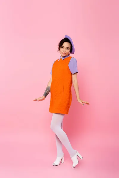 Full length view of positive woman in orange sleeveless dress posing on pink — Stock Photo