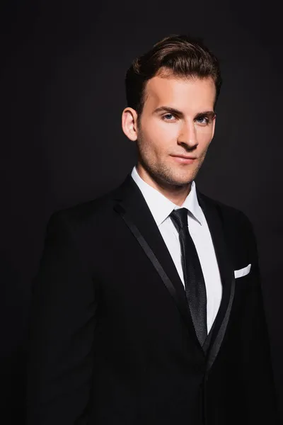 Young confident man in elegant suit looking at camera on black — Stock Photo