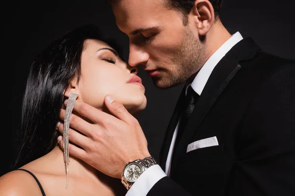 Elegante hombre besando morena mujer aislado en negro - foto de stock