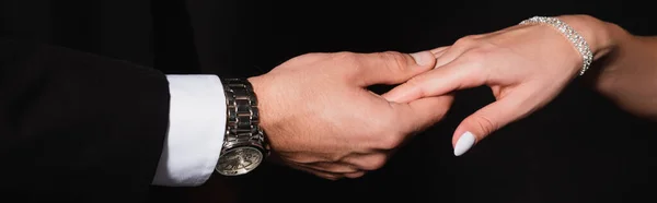 Vista parcial del hombre cogido de la mano de la mujer aislado en negro, bandera — Stock Photo