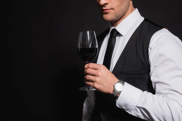 Обрізаний вид елегантного чоловіка, що тримає келих червоного вина ізольовано на чорному — стокове фото