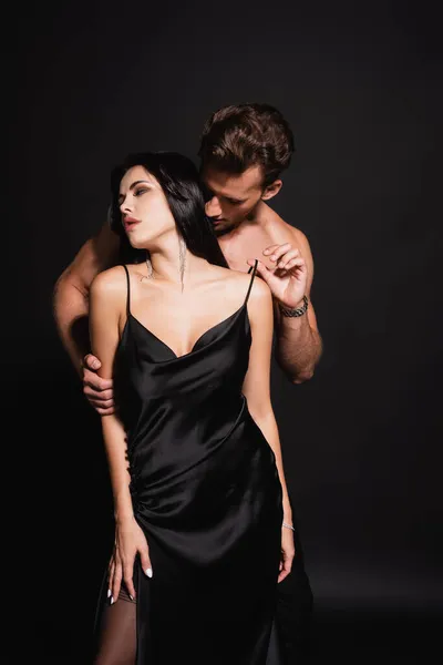 Shirtless man touching strap of silk dress on passionate woman on black — Stock Photo