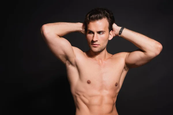 Sexy hombre sin camisa con torso muscular posando con las manos detrás de la cabeza aislado en negro — Stock Photo