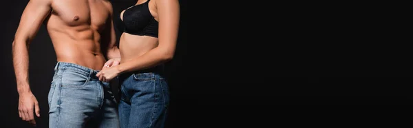 Cropped view of woman in bra undressing shirtless man isolated on black, banner — Stock Photo