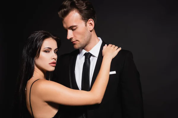 Passionate woman looking at camera near man in elegant suit isolated on black — Stock Photo