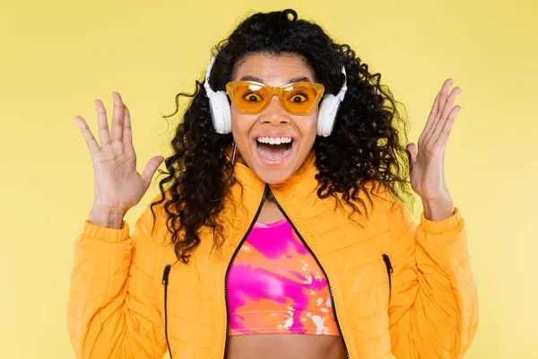 Étonnante jeune femme afro-américaine en lunettes de soleil et écouteurs isolés sur jaune — Photo de stock