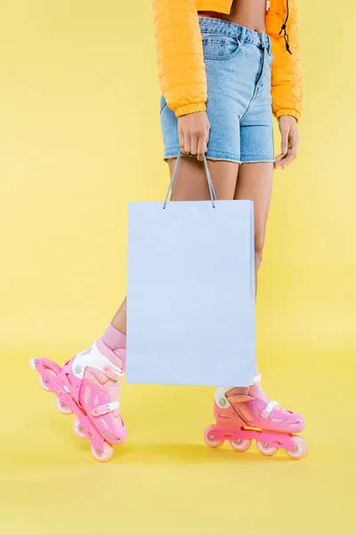 Vista cortada da jovem americana africana em patins segurando saco de compras no amarelo — Fotografia de Stock