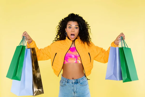 Shocked african american woman holding shopping bags isolated on yellow — Stock Photo