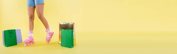 Cropped view of african american woman in roller skates near shopping bags on yellow, banner — Stock Photo