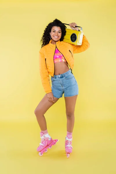 Pleine longueur de femme afro-américaine heureuse sur patins à roulettes tenant boombox rétro sur jaune — Photo de stock