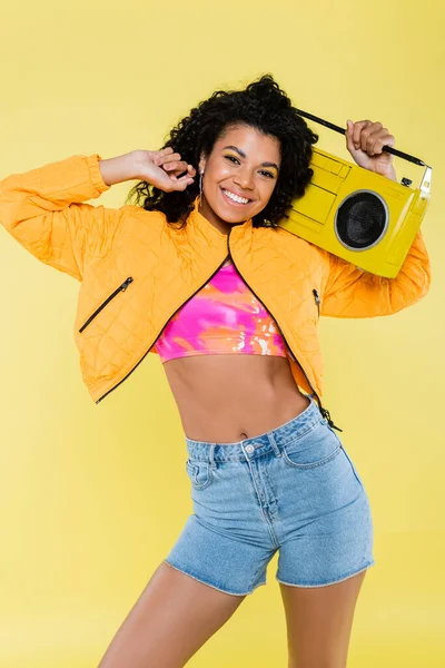 Allegro afro americano giovane donna in possesso di boombox isolato su giallo — Foto stock