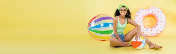 Volle Länge der glücklichen afrikanisch-amerikanischen Frau sitzt mit Strandball auf gelb, Banner — Stockfoto