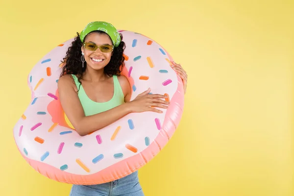 Positive afrikanisch-amerikanische junge Frau steht mit aufblasbarem Ring isoliert auf gelb — Stockfoto