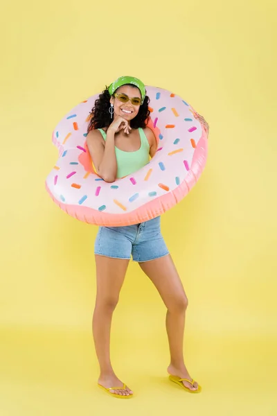 Pleine longueur de jeune femme africaine américaine positive debout avec anneau gonflable sur jaune — Photo de stock