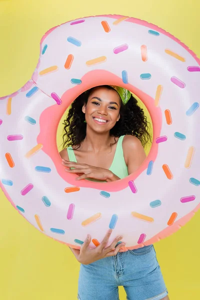 Happy african american young woman holding inflatable ring isolated on yellow — Stock Photo