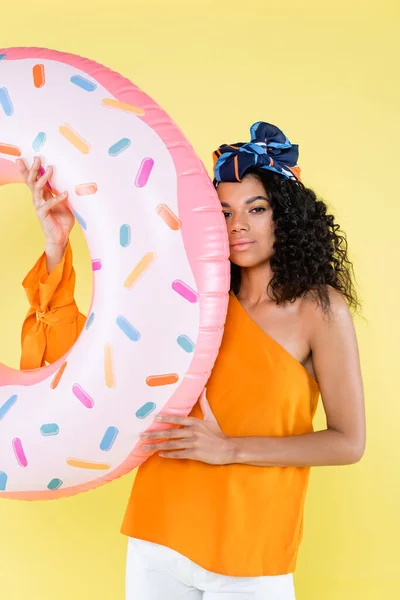 Afro-américaine jeune femme en foulard tenant donut gonflable isolé sur jaune — Photo de stock